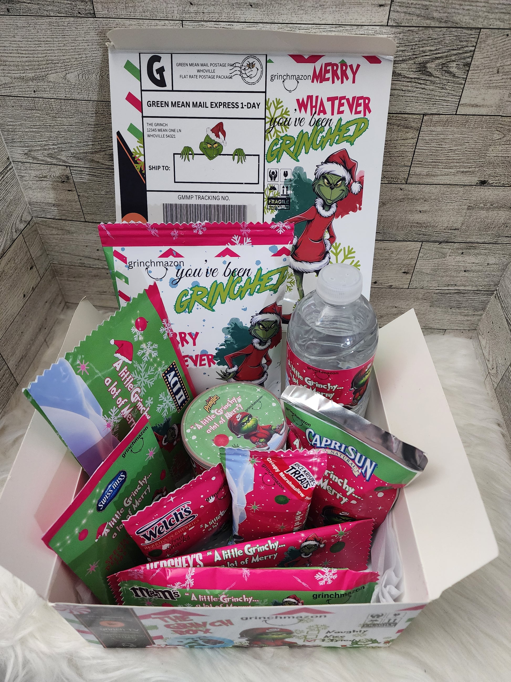 A festive holiday treat box with a custom designed pattern, containing various Christmas themed snacks and a bottled water, placed next to its packaging.